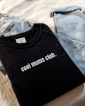Cool Mums Club black tee flat lay with jeans